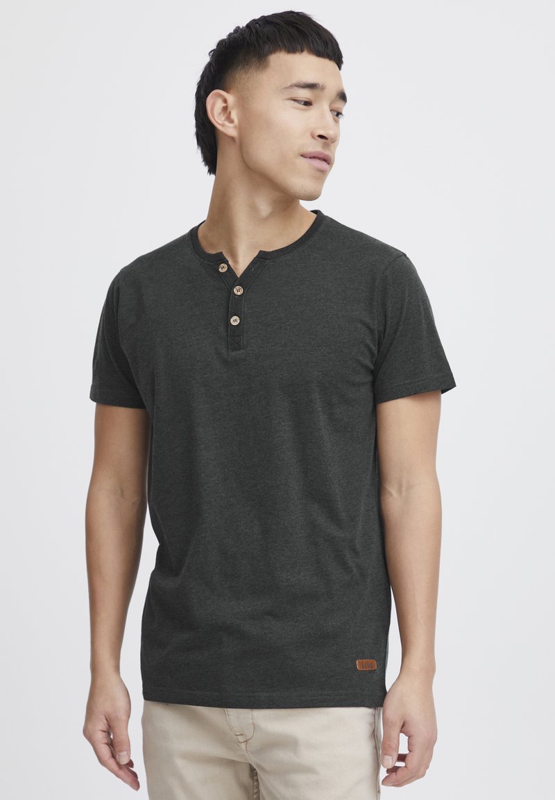 Camiseta henley de manga corta en gris oscuro, fabricada con tejido suave, que cuenta con tres botones de madera en el cuello y una pequeña etiqueta de cuero con la marca en el dobladillo.