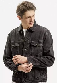 Czarna kurtka dżinsowa z guzikami z przodu, kieszeniami na piersi i regulowanymi mankietami. Ma klasyczny kołnierz i lekko przetartą fakturę.