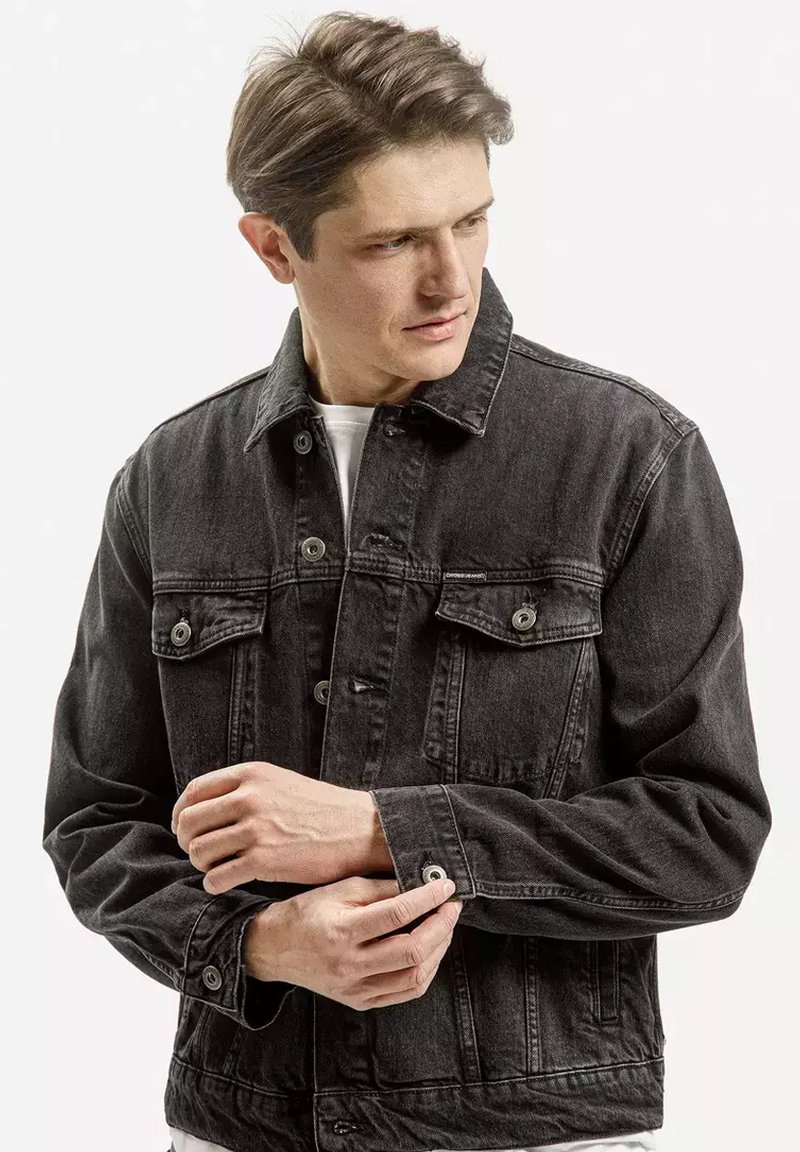 Czarna kurtka dżinsowa z guzikami z przodu, kieszeniami na piersi i regulowanymi mankietami. Ma klasyczny kołnierz i lekko przetartą fakturę.