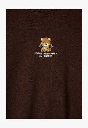 Brązowa bluza z okrągłym dekoltem, z haftowanym niedźwiedziem z skrzydłami i napisem "TY JESTEŚ PROBLEMEM, JA JESTEM IDEALNY" poniżej.
