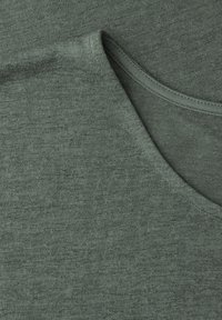 Groen stofdetail met zachte gebreide textuur en een afgeronde halslijn met zichtbare stiknaden.