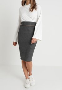 Černobílá sukně ve vzoru houndstooth, doplněná o bílou dlouhousedou halenku a bílé tenisky.