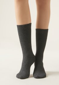 Calcetines gris de canalé hechos de material suave, diseño hasta la rodilla, con un patrón texturizado a lo largo del tubo y una puntera reforzada.