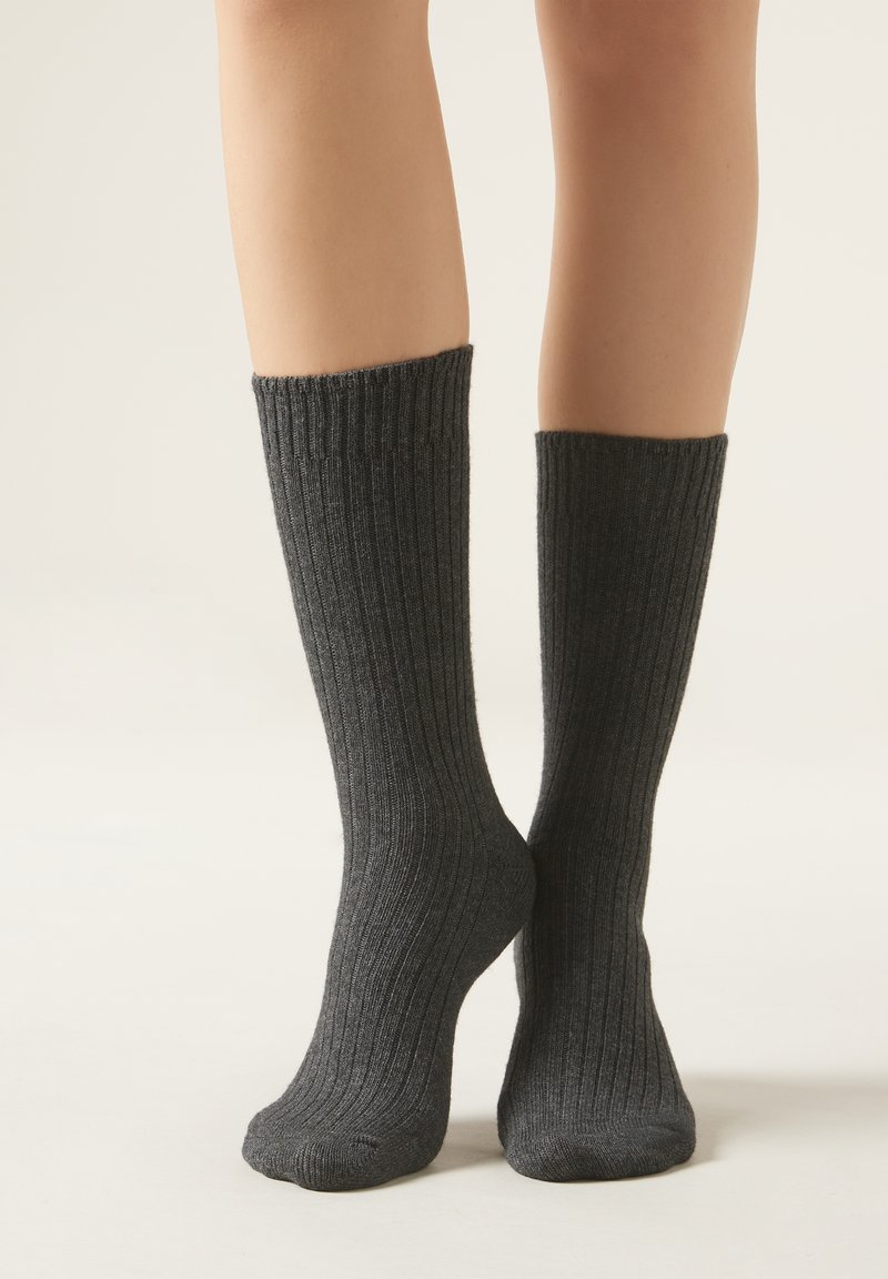 Calcetines gris de canalé hechos de material suave, diseño hasta la rodilla, con un patrón texturizado a lo largo del tubo y una puntera reforzada.