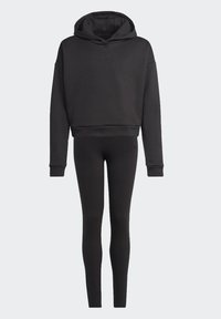 Felpa nera con cappuccio regolabile e cordino, con polsini e orlo a costine. Abbinata a leggings neri, entrambi in un tessuto liscio e elastico.