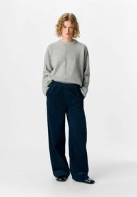 Pull en tricot gris avec un col rond associé à un pantalon large en velours côtelé bleu marine, doté d'une taille élastique et de poches latérales.