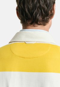 Geel en crèmekleurige pullover met een kraag, met een zachte textuur en een cirkelvormige accent aan de achterkant. Eenvoudig ontwerp en strakke lijnen.