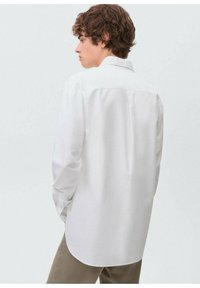 Camicia bianca a maniche lunghe con colletto a punta, polsini abbottonati e orlo dritto. Il tessuto appare liscio con una texture leggera.