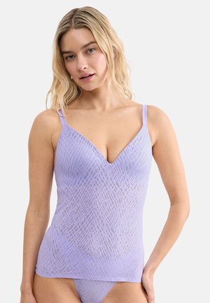 Donna con capelli biondi fino alle spalle che indossa una canottiera leggera viola chiaro trasparente con motivi e biancheria intima abbinata su uno sfondo semplice.