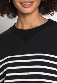 Schwarz-weißer gestreifter Pullover mit weicher Textur, ausgestattet mit einem V-Ausschnitt und gerippten Bündchen. Nahaufnahme zeigt die Stoffdetails.