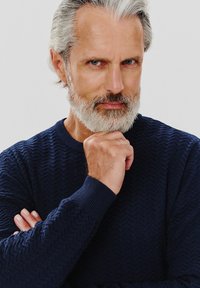 Granatowy sweter z teksturowanej dzianiny, z wzorem w zygzaki, prążkowanymi mankietami i okrągłym dekoltem, noszony przez osobę z siwymi włosami i brodą.