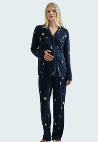 Conjunto de pijama azul marino en tela suave que presenta patrones celestiales de lunas, soles y estrellas. Mangas largas y pantalones holgados.