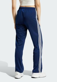 Pantalones deportivos de color azul marino con un corte relajado, con franjas blancas a los lados y una cinturilla elástica. Tejido suave y texturizado.