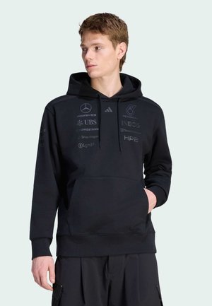 Schwarzer Kapuzenpullover aus weichem Stoff, mit einer Kängurutasche vorne und verschiedenen Logos in dunklen Tönen auf Vorderseite und Ärmeln bedruckt.