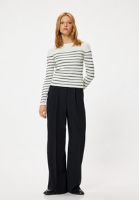 Gestreepte witte lange mouw top met zwarte horizontale strepen, gecombineerd met hoge zwarte wijde broek. Zwarte schoenen maken de outfit compleet.