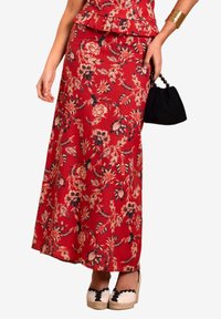 Rode bloemen maxi rok met een peplum top, voorzien van zwarte bloemaccenten, en gecombineerd met crèmekleurige espadrilles. Inclusief een kleine zwarte handtas.