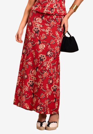 Rote Maxi-Rock mit floralen Mustern, kombiniert mit einem Peplum-Oberteil, das schwarze florale Akzente aufweist, und dazu beigen Espadrilles. Enthält eine kleine schwarze Handtasche.