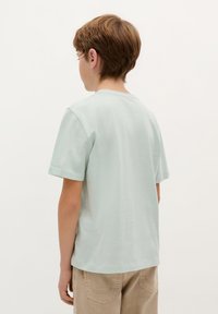 Mintgroene katoenen T-shirt met korte mouwen, een ronde halslijn en een relaxte pasvorm, gecombineerd met lichtbeige broek. Achteraanzicht.
