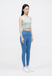 Szürke, rövidített atléta és kék, magas derekú leggings sima anyagból, fehér tornacipővel párosítva. A modell oldalról áll, egyszínű háttér előtt.