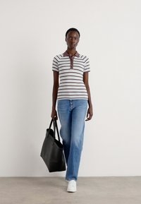 Stripet polo-shirt i hvit med brune detaljer, kombinert med lyseblå jeans og hvite joggesko. Modellen holder en svart totebag.