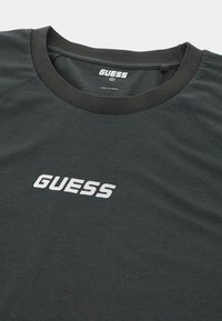 Tamsiai žalia marškinėliai su apvaliu kaklu, su baltu "GUESS" logotipu ant krūtinės. Pagaminti iš minkštos, lengvos medžiagos.