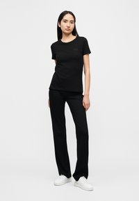 Μαύρο βαμβακερό μπλουζάκι με κοντά μανίκια και στρογγυλή λαιμόκοψη, συνδυασμένο με μαύρο παντελόνι. Και τα δύο ρούχα έχουν εφαρμοστή γραμμή. Το σύνολο ολοκληρώνεται με λευκά αθλητικά παπούτσια.