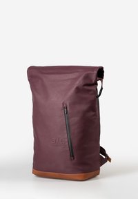 Lila Leder Rucksack mit Roll-Top-Design, ausgestattet mit einem schwarzen Reißverschluss, einem braunen Lederboden und dezentem Branding auf der Vorderseite.