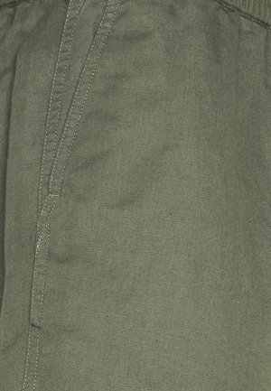 Gros plan sur un tissu vert avec tissage diagonal visible et coutures renforcées le long de la couture et du bord de la poche.