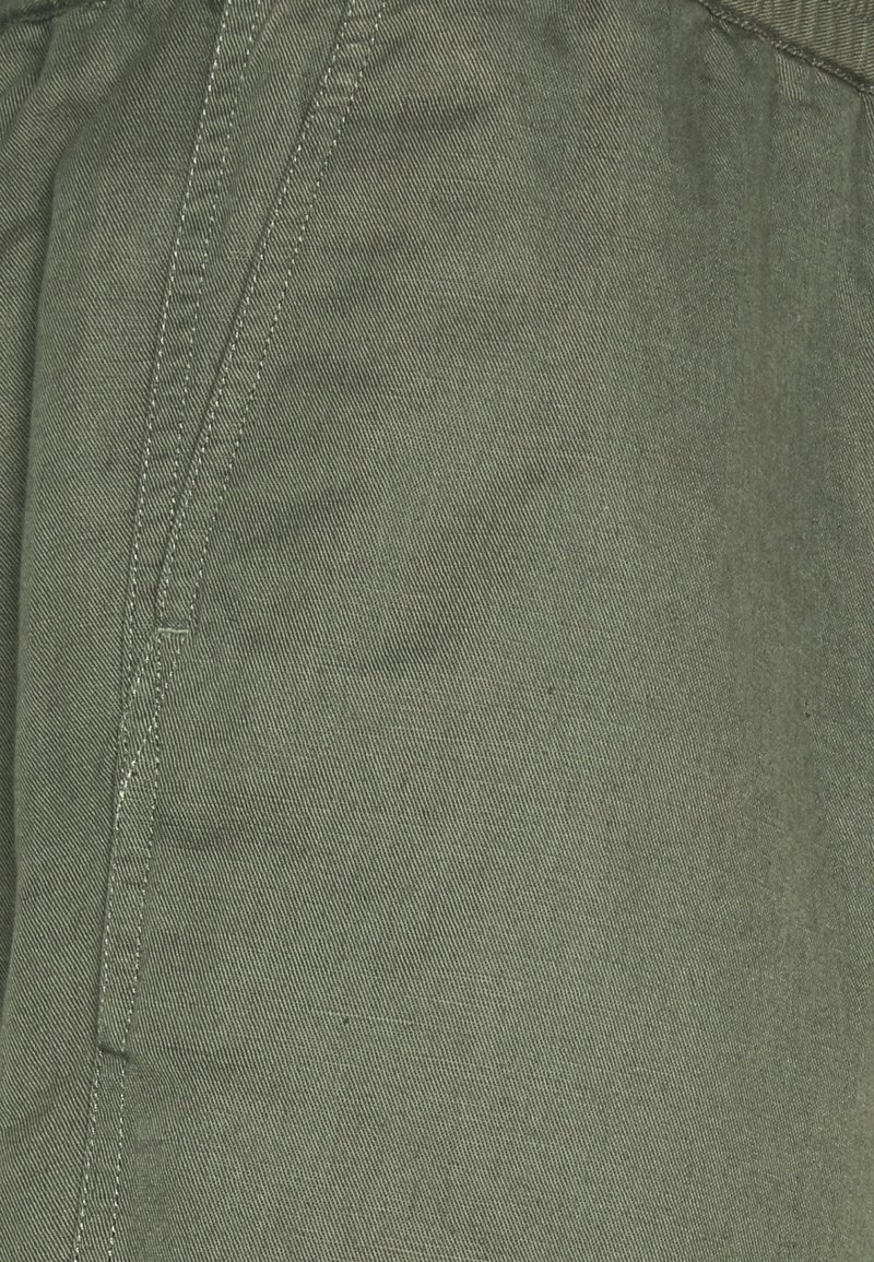Gros plan sur un tissu vert avec tissage diagonal visible et coutures renforcées le long de la couture et du bord de la poche.