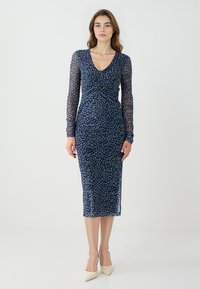 Abito blu navy con maniche lunghe trasparenti, davanti arricciato e motivo a pois multicolore. Design aderente, lunghezza al ginocchio con silhouette dritta.