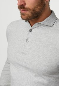 Polo a maniche lunghe grigio con una texture morbida, dotato di colletto, tre bottoni e dettagli di cucitura sottili. Vista ravvicinata che mostra la qualità del tessuto.