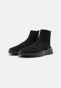 Baskets noires en tricot montantes à la cheville avec un dessus texturé, des languettes de tirage et des semelles rembourrées, conçues pour le confort et la flexibilité.