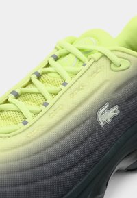 Baskets dégradé jaune néon et gris avec dessus en mesh, col rembourré et logo crocodile sur le côté près de la semelle noire.