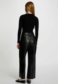 Maglia nera a costine con maniche lunghe abbinata a pantaloni larghi in pelle nera a vita alta, con tasche posteriori e scarpe basse.