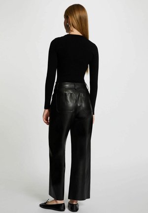 Maglia nera a costine con maniche lunghe abbinata a pantaloni larghi in pelle nera a vita alta, con tasche posteriori e scarpe basse.