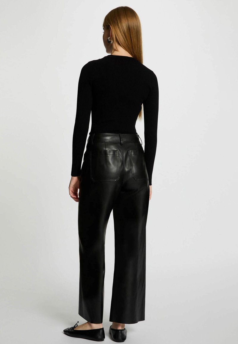 Maglia nera a costine con maniche lunghe abbinata a pantaloni larghi in pelle nera a vita alta, con tasche posteriori e scarpe basse.