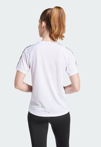 T-shirt blanc à manches courtes avec des accents noirs sur les épaules, texture douce et coupe décontractée, associé à un legging noir.