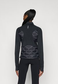 Jaqueta atlética preta com um topo justo, mangas longas e um painel inferior acolchoado. Tecido suave com um brilho subtil.