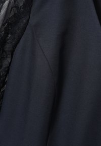 Navy Kleid aus glattem Stoff mit einer strukturierten Spitzenüberlagerung auf der linken Seite. Das Design umfasst eine taillierte Silhouette und einen leichten Glanz.