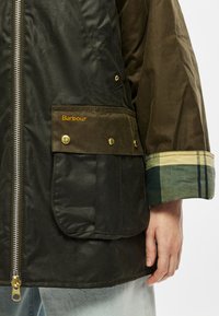 Μπουφάν Barbour με εξωτερικό μέρος σε σκ�ούρο πράσινο, φερμουάρ μπροστά και μανσέτες με καρό σχέδιο σε γήινες αποχρώσεις. Περιλαμβάνει δύο τσέπες με κουμπιά τύπου snap.