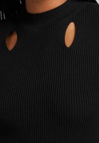 Svart ribbad topp med hög hals; har två ovala utskärningar vid axlarna. Tillverkad av mjukt, texturerat tyg.