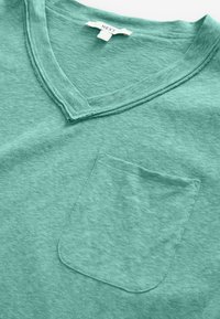 Zelené tričko s výstrihom do V, vyrobené z mäkkej bavlny, s jedným náprsným vreckom a textúrovaným, mierne melírovaným povrchom.