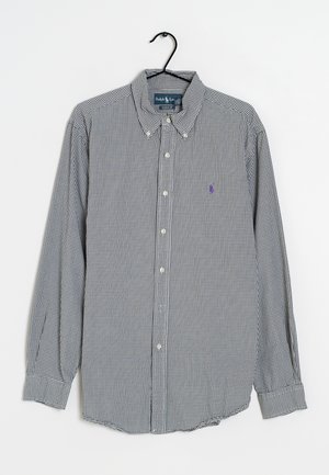 Camicia a maniche lunghe a quadri bianco e nero con colletto, appesa a una gruccia nera su uno sfondo semplice.
