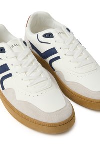 Sneakers bianchi con strisce blu navy, dettagli in suede testurizzato e suola in gomma naturale. Presentano chiusura con lacci e dettagli perforati sulla punta.