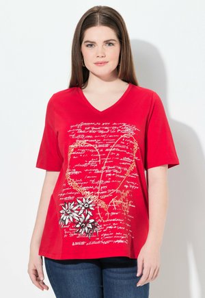 T-shirt rouge à manches courtes en V, présentant un motif floral avec des marguerites blanches et des motifs de texte manuscrit. Fabriqué en tissu de coton.