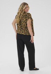 Leopardmuster Kurzarmoberteil in Braun und Schwarz, kombiniert mit weiten schwarzen Hosen. Glatte Textur mit entspannter Passform.