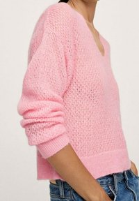 Pull en maille rose clair avec col en V, manches longues et poignets côtelés ; présente une texture ouverte et aérée ainsi qu'une silhouette courte.
