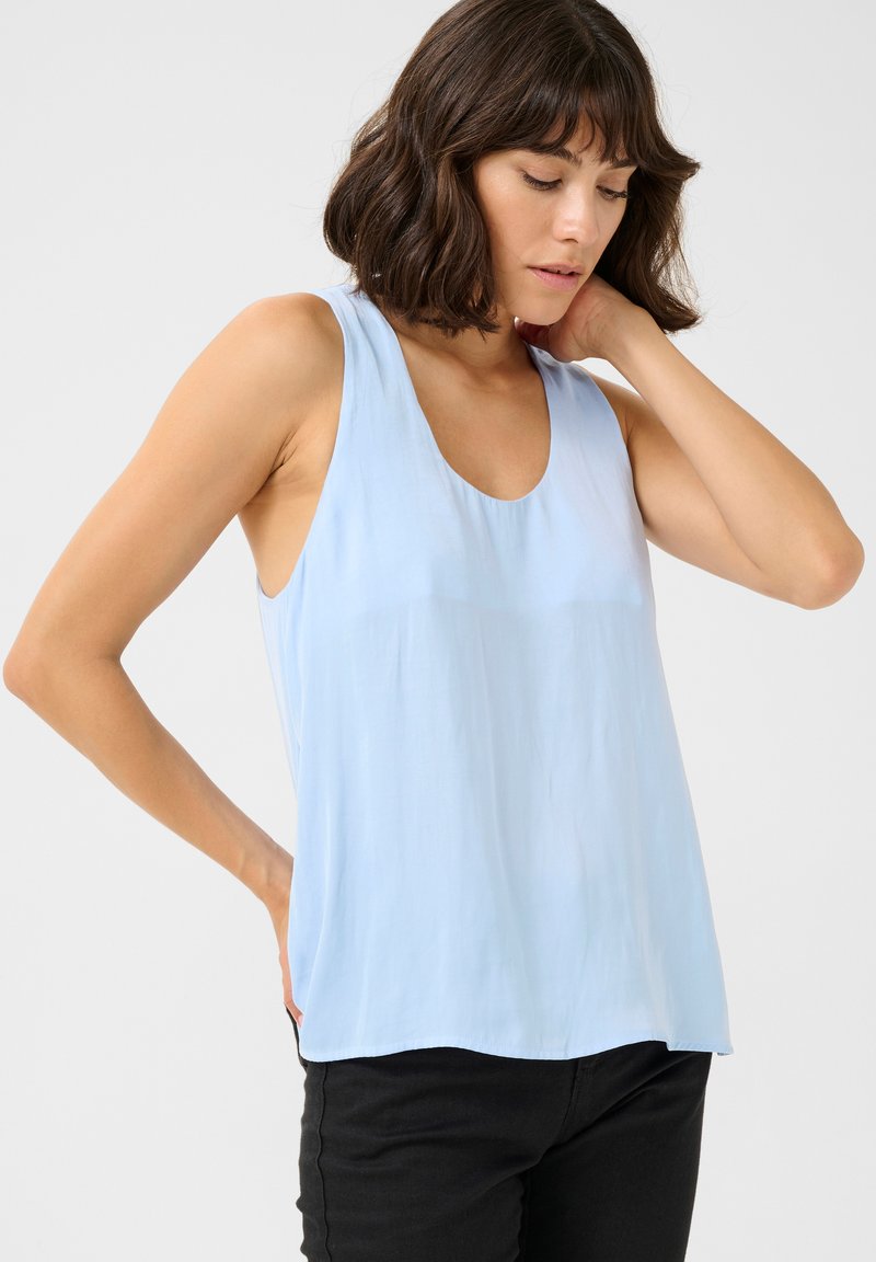 Haut sans manches bleu clair en tissu doux et transparent, avec un décolleté bateau et une coupe décontractée, accompagné de pantalons noirs. Texture lisse.