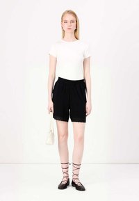 White short-sleeve shirt paired with black shorts featuring lace trim. Model wears black flats and holds a small white handbag.