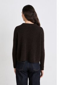 Brown, fuzzy knit sweater with a rounded neckline and dropped shoulders, paired with indigo denim jeans featuring back pockets and stitching.
